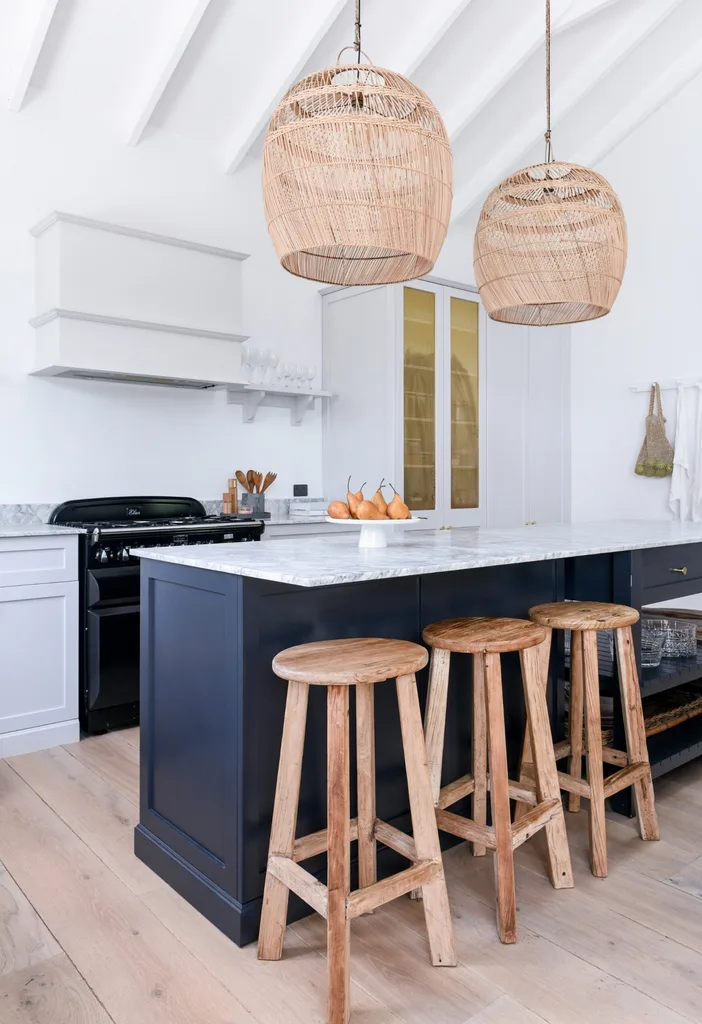 Kitchen with marble island, wooden stools, wicker pendant lights, and light wood flooring.