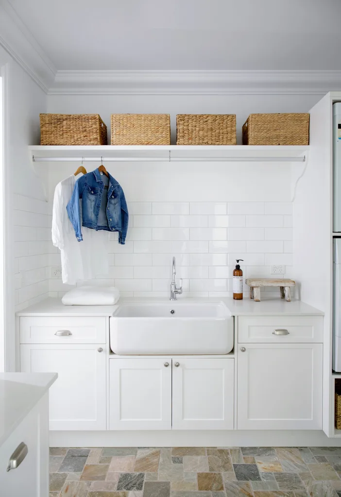 Laundry room with white cabinets, farmhouse sink, hanging denim jacket, wicker baskets on shelf, and herringbone tile floor. combined bathroom and laundry