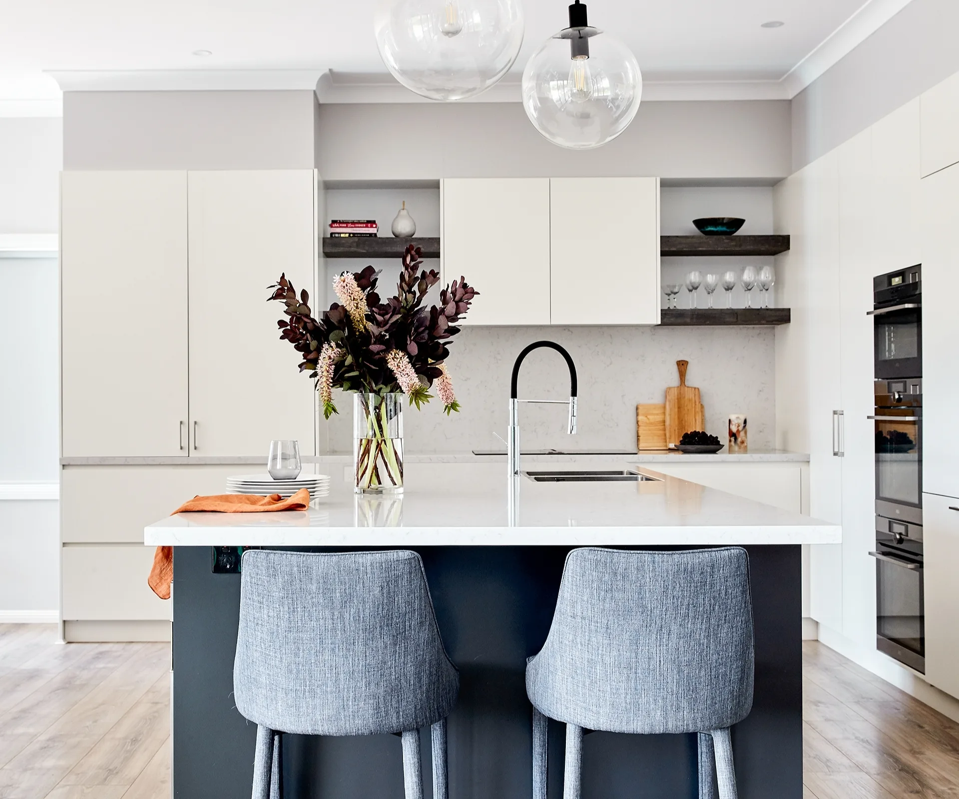 Modern kitchen with a white island, two gray chairs, a vase of flowers, and pendant lights.