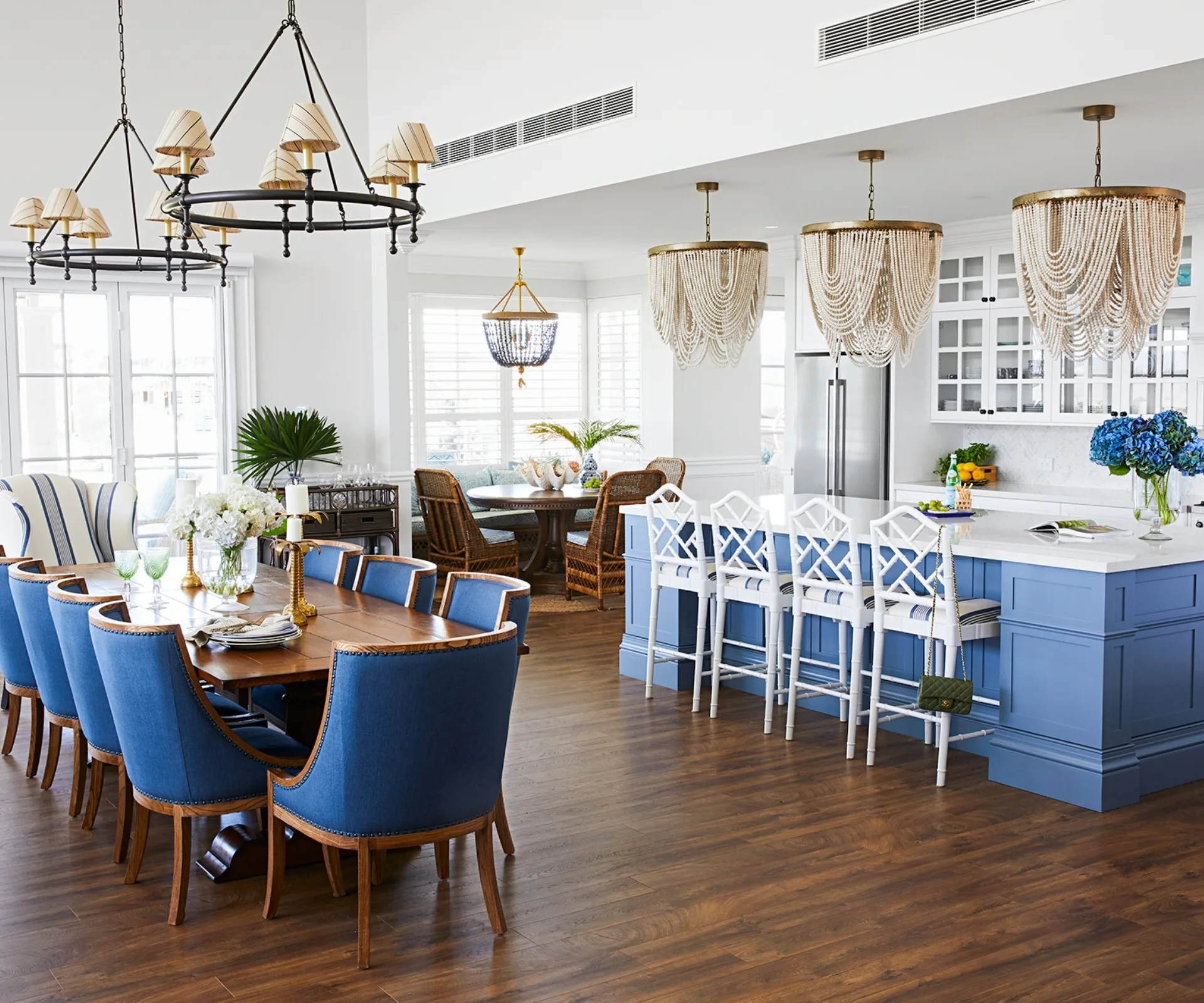 Coastal-style kitchen and dining area with blue and white decor, wooden floors, and elegant chandeliers.