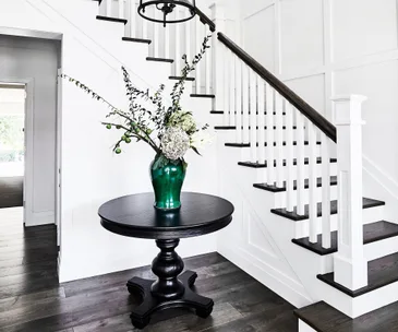 Entryway with a black round table, green vase with flowers, wooden staircase, and white walls.