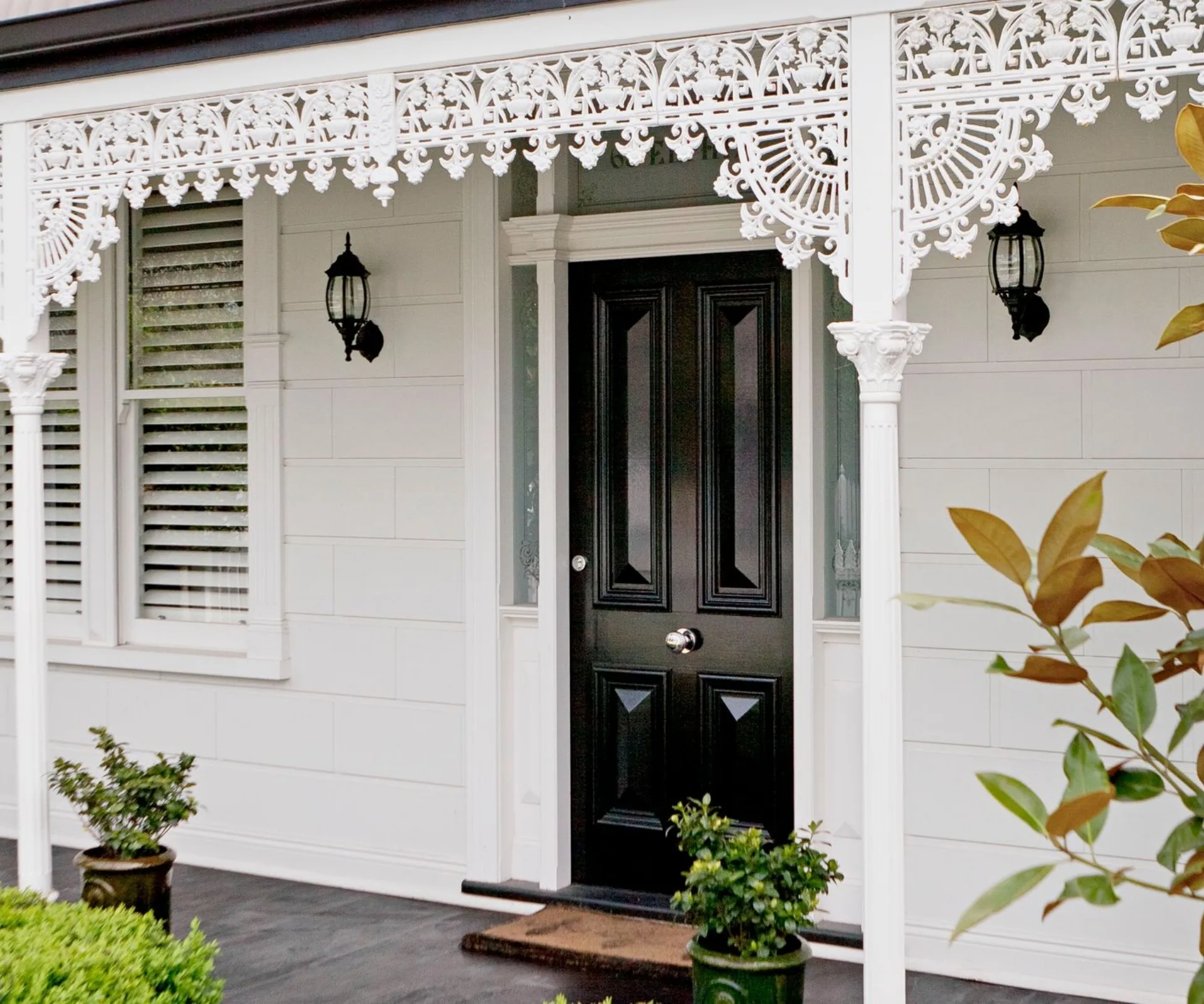 Front view of a house with decorative white trim, black door, and potted plants.