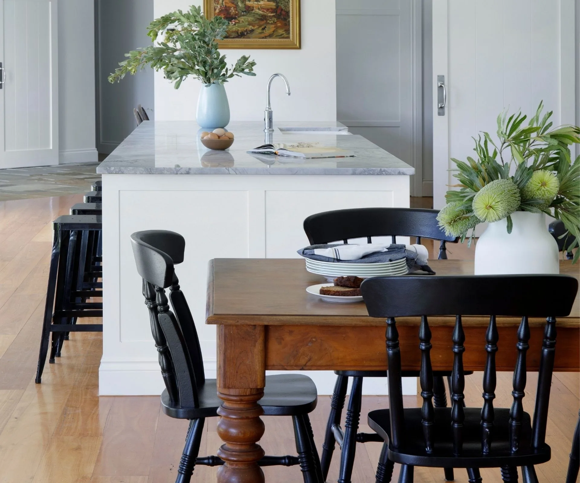 Kitchen with wooden floor, black chairs, wooden dining table, and a white countertop with green plant decor.