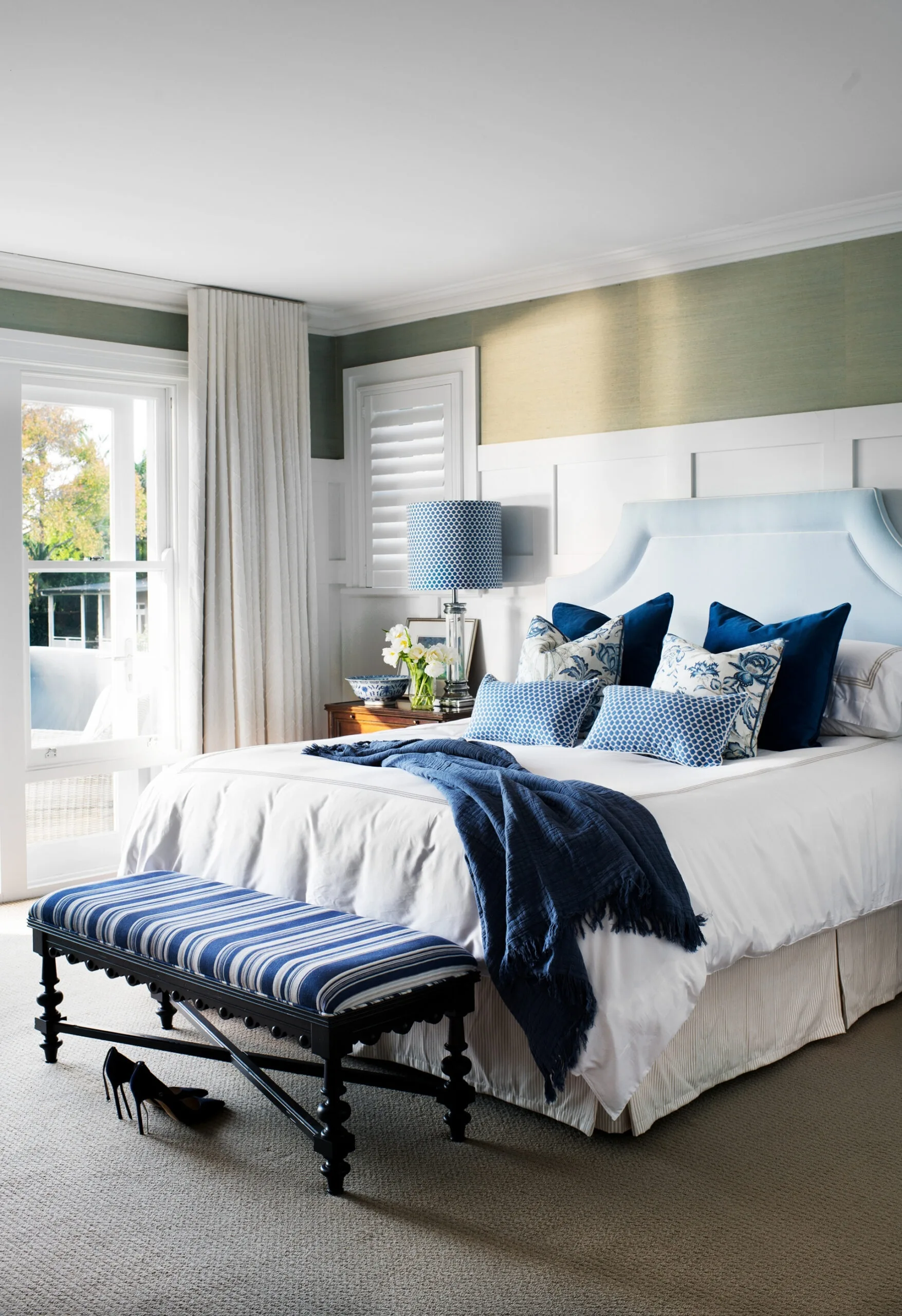Cozy bedroom with a blue and white theme, featuring a cushioned headboard, bench, and a pair of high-heeled shoes.