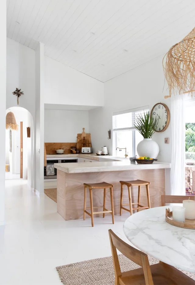 Coastal white kitchen with rattan pendant and timber stools