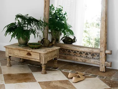 Rustic mirror with green panel beside table holding plants and rooster figurine, on checkered tile floor.