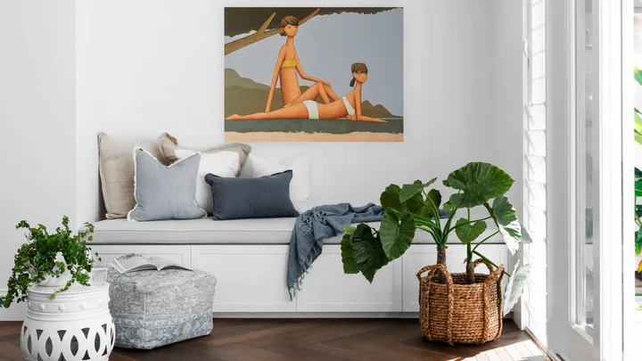 Cozy white corner with cushions and painting, herringbone wood floor, large leafy plant, and natural light from windows.