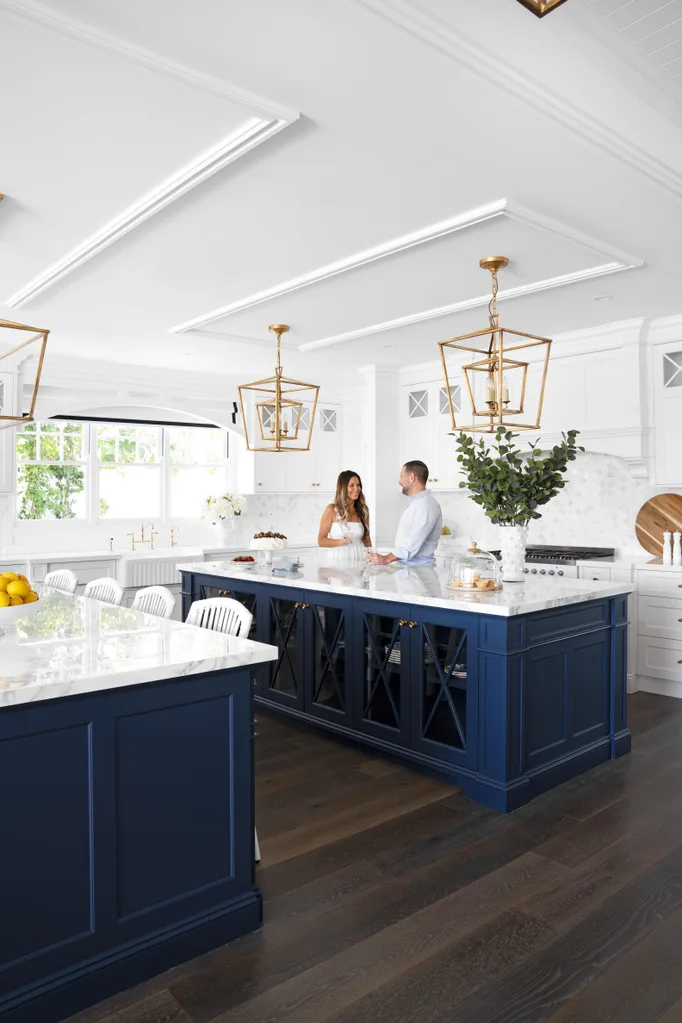 Bright kitchen with blue island, gold lighting fixtures, and two people conversing by the counter.