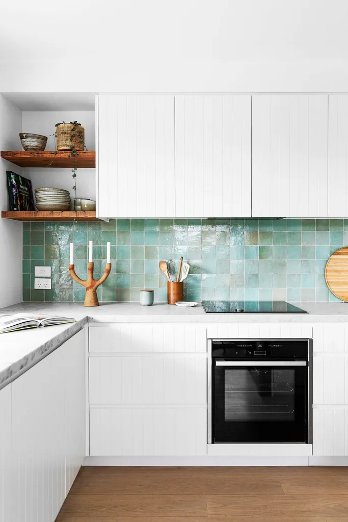 Modern kitchen with white cabinets, green tile backsplash, wooden shelves, and a black oven.