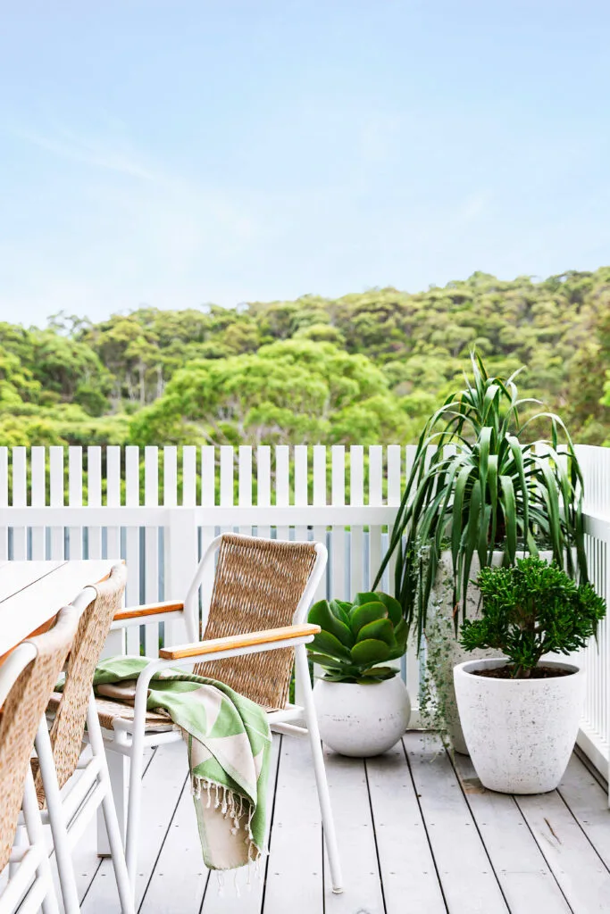 Small coastal balcony with dining table and cluster of three pots filled with succulents.