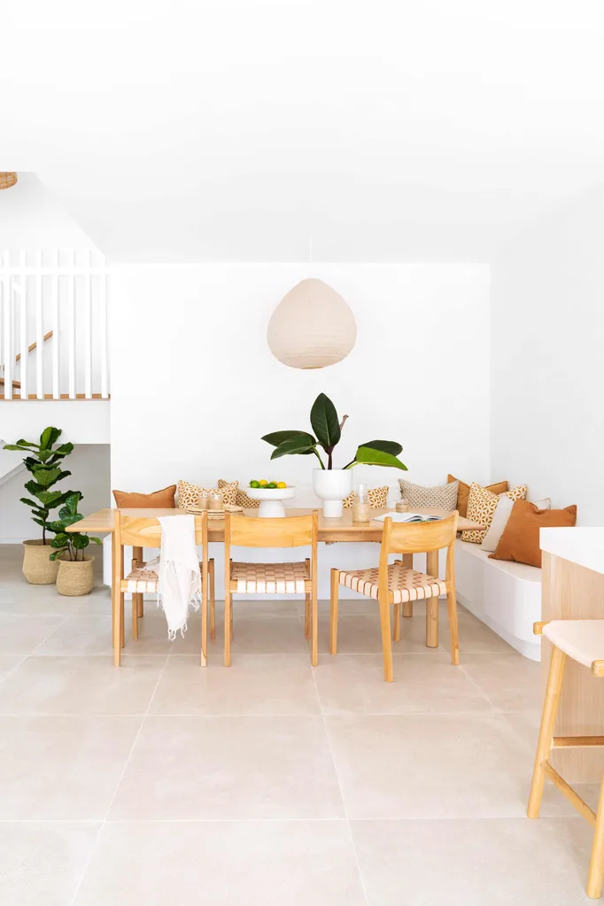 Modern dining area with a light wooden table, chairs, neutral decor, green plant centerpiece, and a hanging lamp. killing fiddle leaf fig