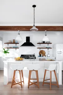 Modern kitchen with white cabinetry, island, wooden stools, and pendant lights. Open shelving and black stove present.