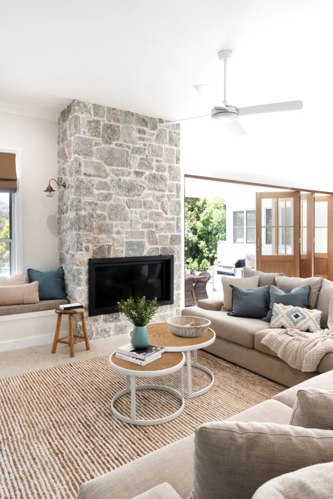 A modern farmhouse living room with a stone fireplace and chunky knit blanket throw on a lounge.