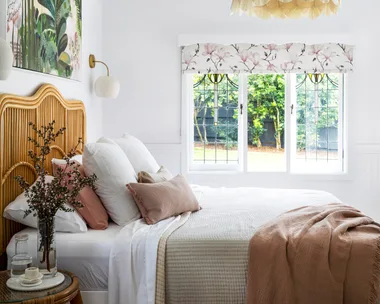 MAIN BEDROOM Tie it all together. Shades of pink, green and white in an artwork by Anna Rodman work wonderfully with the'Carnival' blind in Magnolia Rose from Above & Beyond Shade Solutions. A 'Petal Dome' pendant by Bisque Traders ties in with layered bedlinen from Adairs, No Chintz and In The Sac, as well as the 'Georgia' rattan bedhead from Adairs.