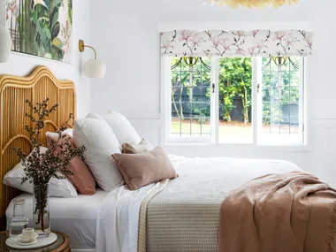 MAIN BEDROOM Tie it all together. Shades of pink, green and white in an artwork by Anna Rodman work wonderfully with the'Carnival' blind in Magnolia Rose from Above & Beyond Shade Solutions. A 'Petal Dome' pendant by Bisque Traders ties in with layered bedlinen from Adairs, No Chintz and In The Sac, as well as the 'Georgia' rattan bedhead from Adairs.