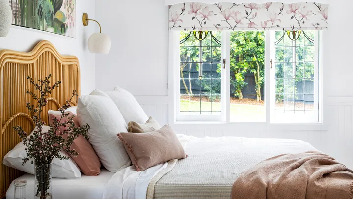 MAIN BEDROOM Tie it all together. Shades of pink, green and white in an artwork by Anna Rodman work wonderfully with the'Carnival' blind in Magnolia Rose from Above & Beyond Shade Solutions. A 'Petal Dome' pendant by Bisque Traders ties in with layered bedlinen from Adairs, No Chintz and In The Sac, as well as the 'Georgia' rattan bedhead from Adairs.