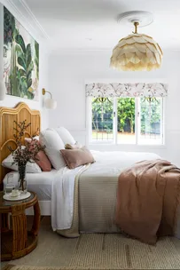 MAIN BEDROOM Tie it all together. Shades of pink, green and white in an artwork by Anna Rodman work wonderfully with the'Carnival' blind in Magnolia Rose from Above & Beyond Shade Solutions. A 'Petal Dome' pendant by Bisque Traders ties in with layered bedlinen from Adairs, No Chintz and In The Sac, as well as the 'Georgia' rattan bedhead from Adairs.