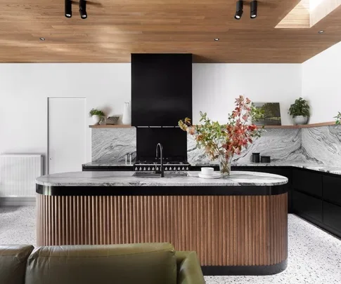 Modern kitchen with wood accents, marble countertops, and a central island with a vase of colorful leaves.