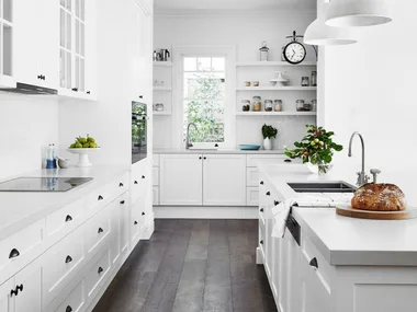 Brushed chrome tapware echoes overhead pendants, yet takes a back seat to other design features in this renovated Federation kitchen with white joinery, white benchtops and white pendant lighting above the kitchen island.
