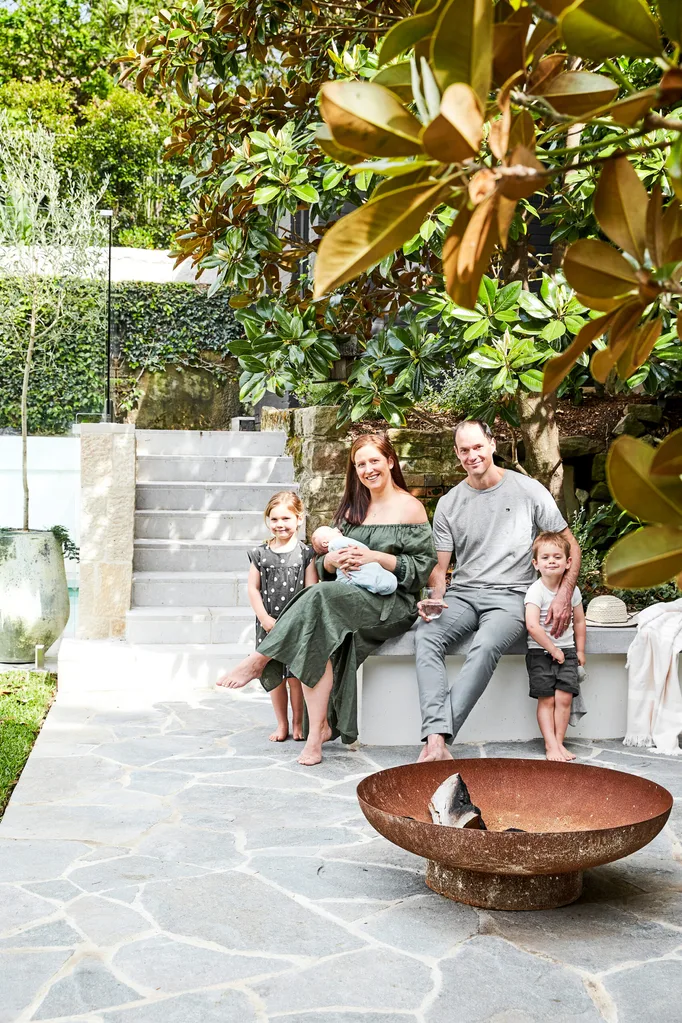 Family sitting on a garden bench with three children, surrounded by lush greenery and a fire pit in the foreground.