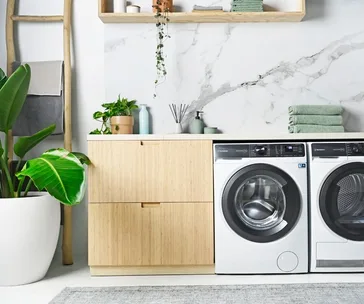 Modern laundry room with plants, wooden cabinet, washer, dryer, and white marble wall.