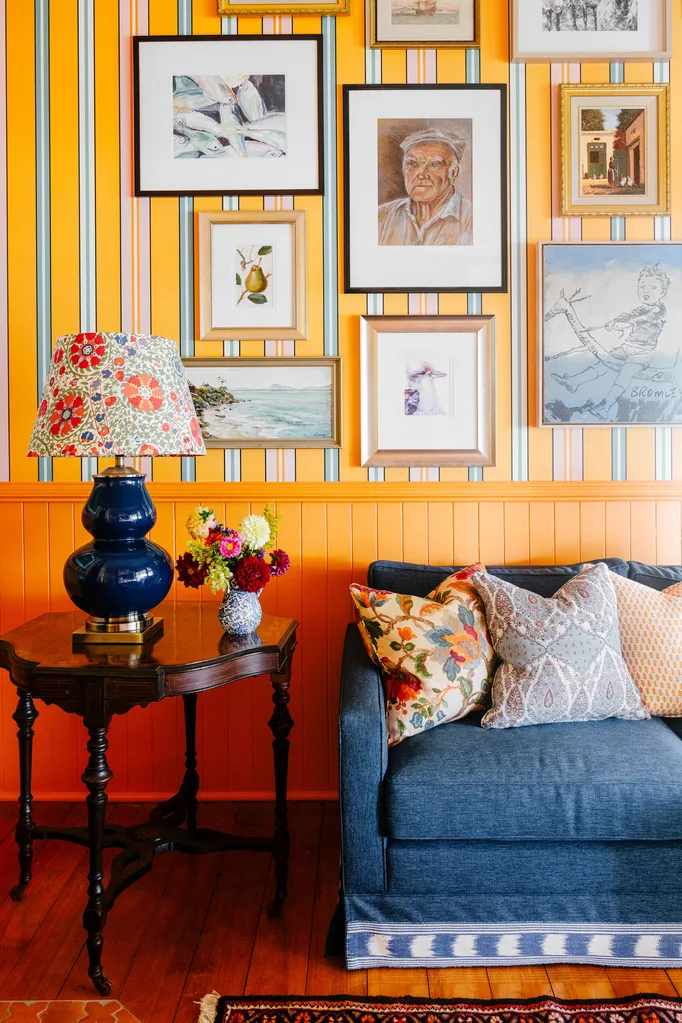 Living room with yellow and blue striped wallpaper, a blue couch and a blue lamp on an antique side table with a patterned lampshade.