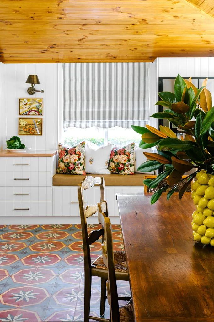Cozy kitchen with floral cushions, patterned tiles, wooden ceiling, and a vase with leaves on a wooden table.