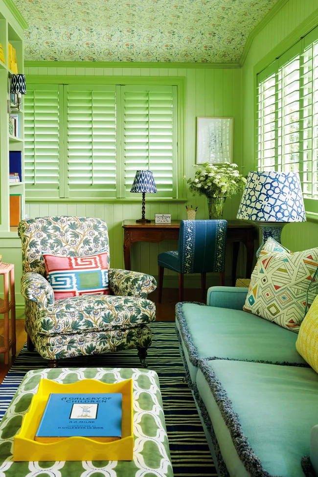 Cozy living room with green walls, floral chair, blue sofa, and patterned ceiling; eclectic and vibrant decor.