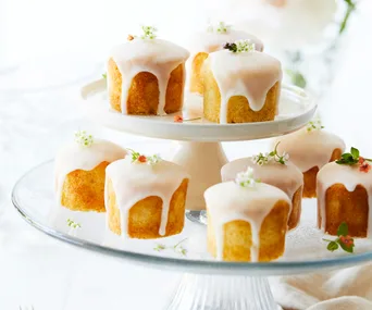 Mini cakes with white icing and flower decorations on a tiered stand.