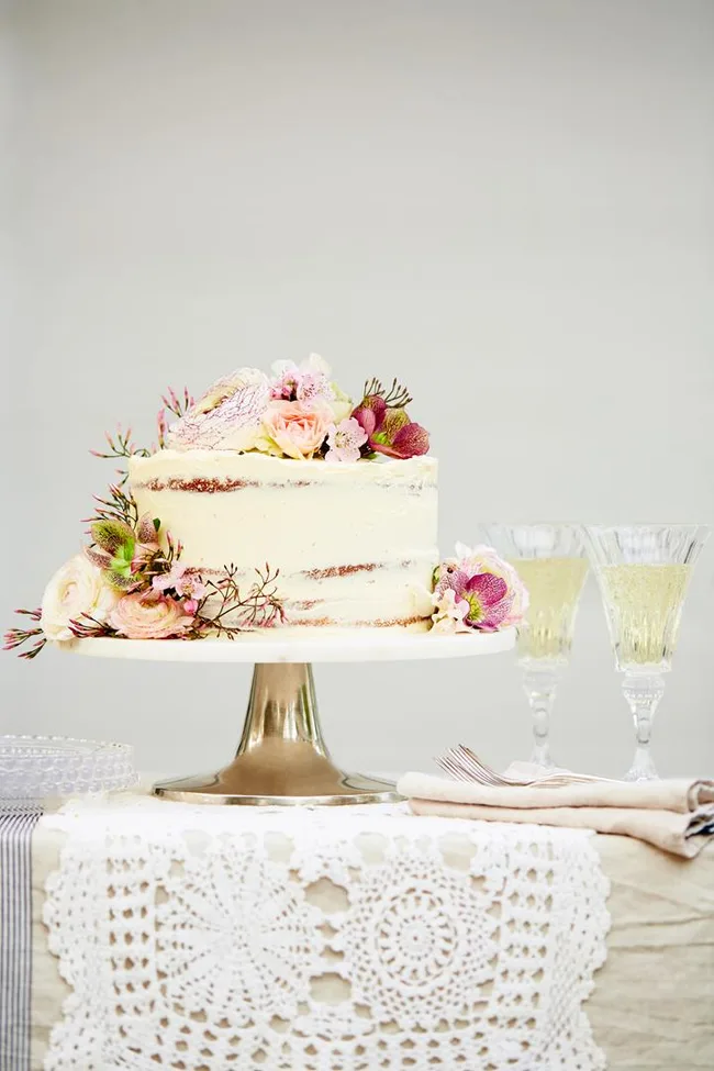 Wedding cake with creamy frosting and floral decorations on a stand, flanked by two glasses of champagne.