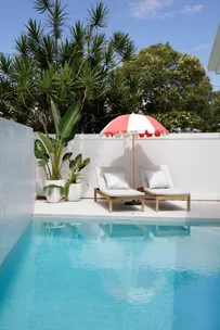 Two lounge chairs beside a pool with a red and white umbrella on a sunny day.