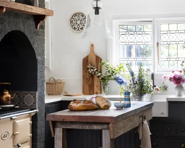 Rustic kitchen with a wooden island, bread, flowers, vintage stove, and a hanging glass light fixture.