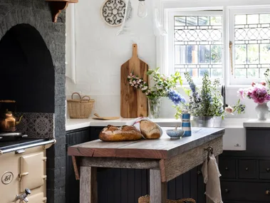 Rustic kitchen with a wooden island, bread, flowers, vintage stove, and a hanging glass light fixture.