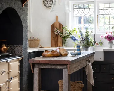Rustic kitchen with a wooden island, bread, flowers, vintage stove, and a hanging glass light fixture.