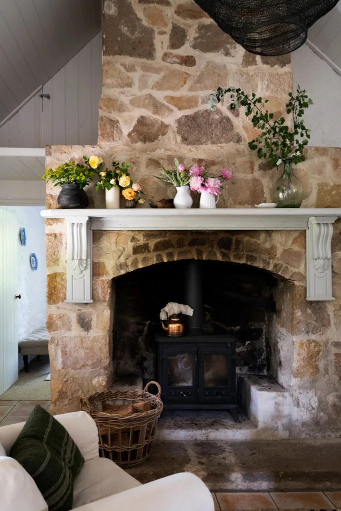 Stone fireplace with mantel decorated with vases of flowers, a wicker basket, and a cozy room setting.