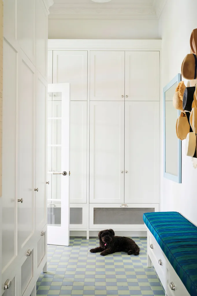 White hallway with built-in cabinets, a blue bench, and a black dog lying on checkered tiles.
