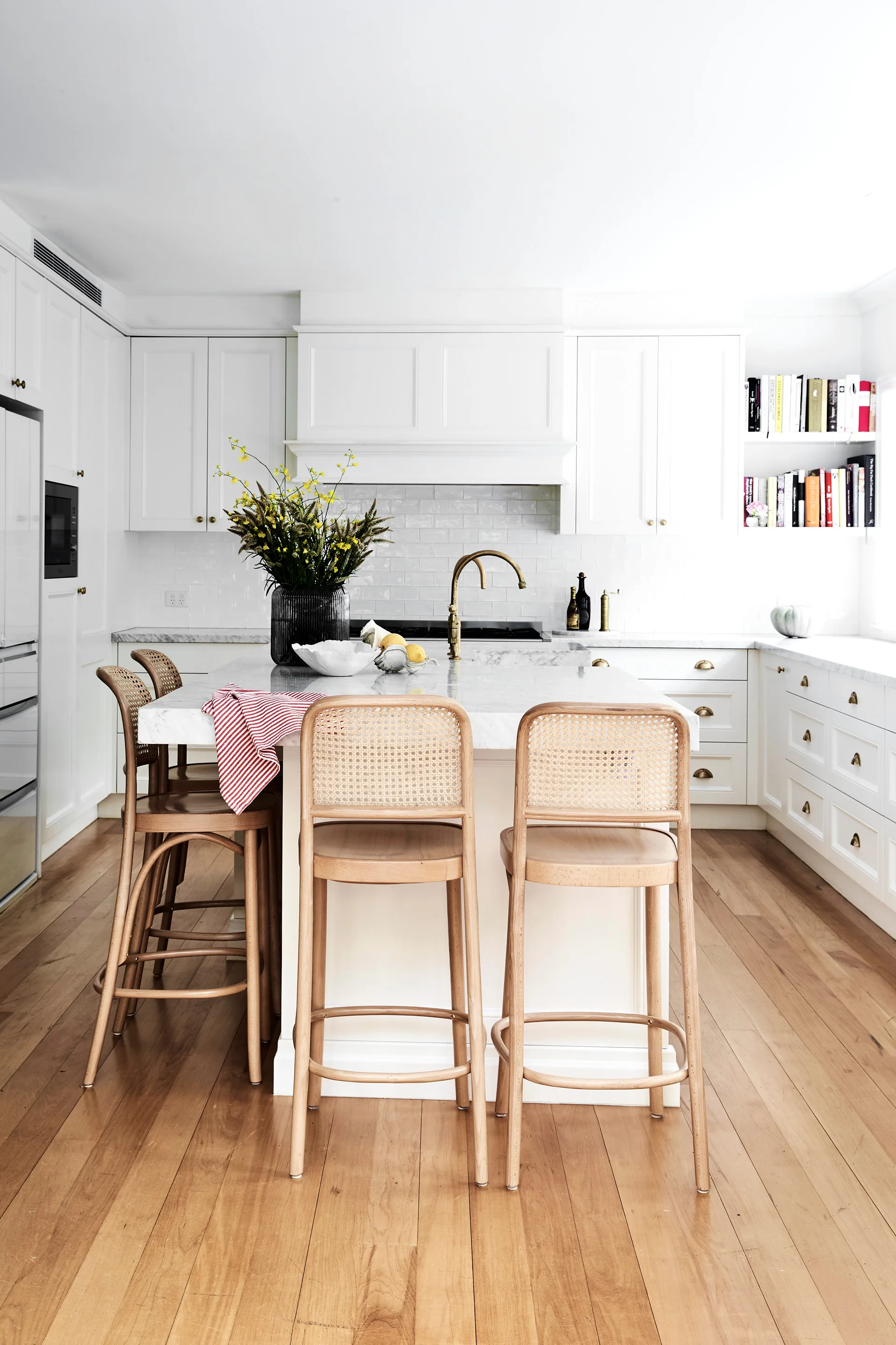 White kitchen with subway tiles, stone benchtops and open shelving with cookbooks displayed.