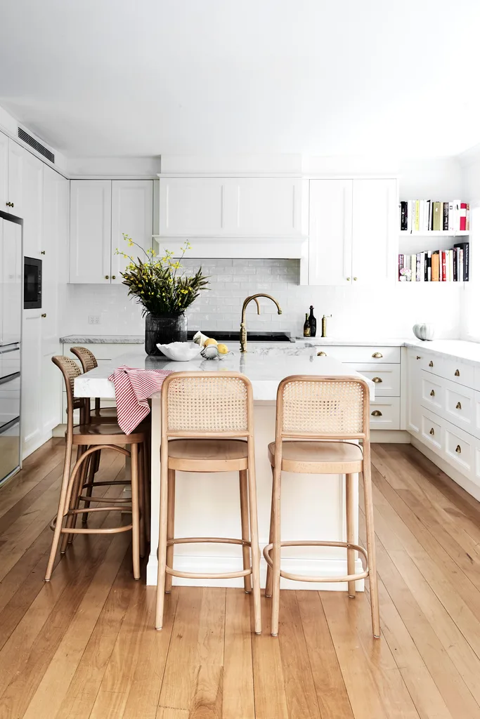 White kitchen with subway tiles, stone benchtops and open shelving with cookbooks displayed.
