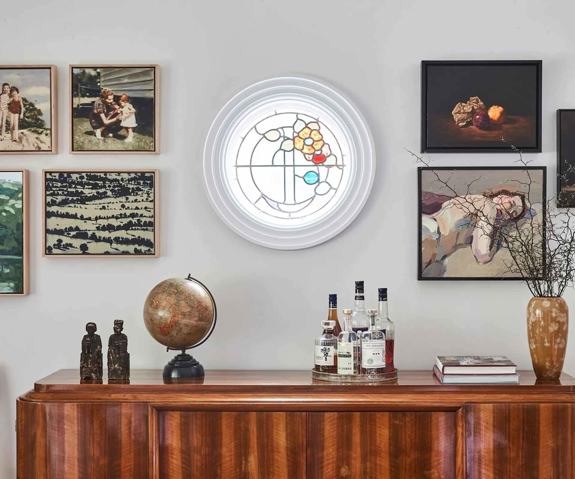 Art-filled living room with a round stained glass window, globe, statues, and a collection of liquor bottles on a wooden cabinet.