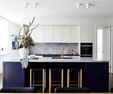 Modern kitchen with white cabinets and navy island base and Miele ovens