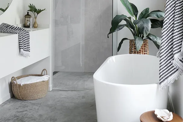 Modern bathroom with a white freestanding bathtub, wicker basket, indoor plant, and black-and-white striped towel.