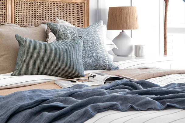 Cozy bedroom with a striped bedspread, blue and beige pillows, a magazine, and a lamp on a white side table.
