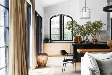 Modern kitchen with black windows, wooden cabinetry, and a potted plant near dining area with black chair.