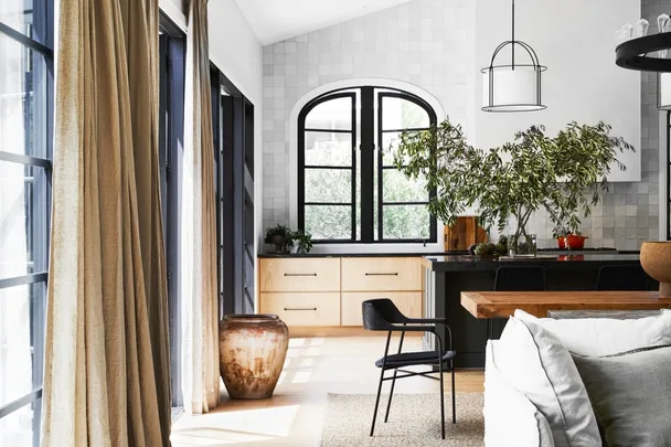 Modern kitchen with black windows, wooden cabinetry, and a potted plant near dining area with black chair.
