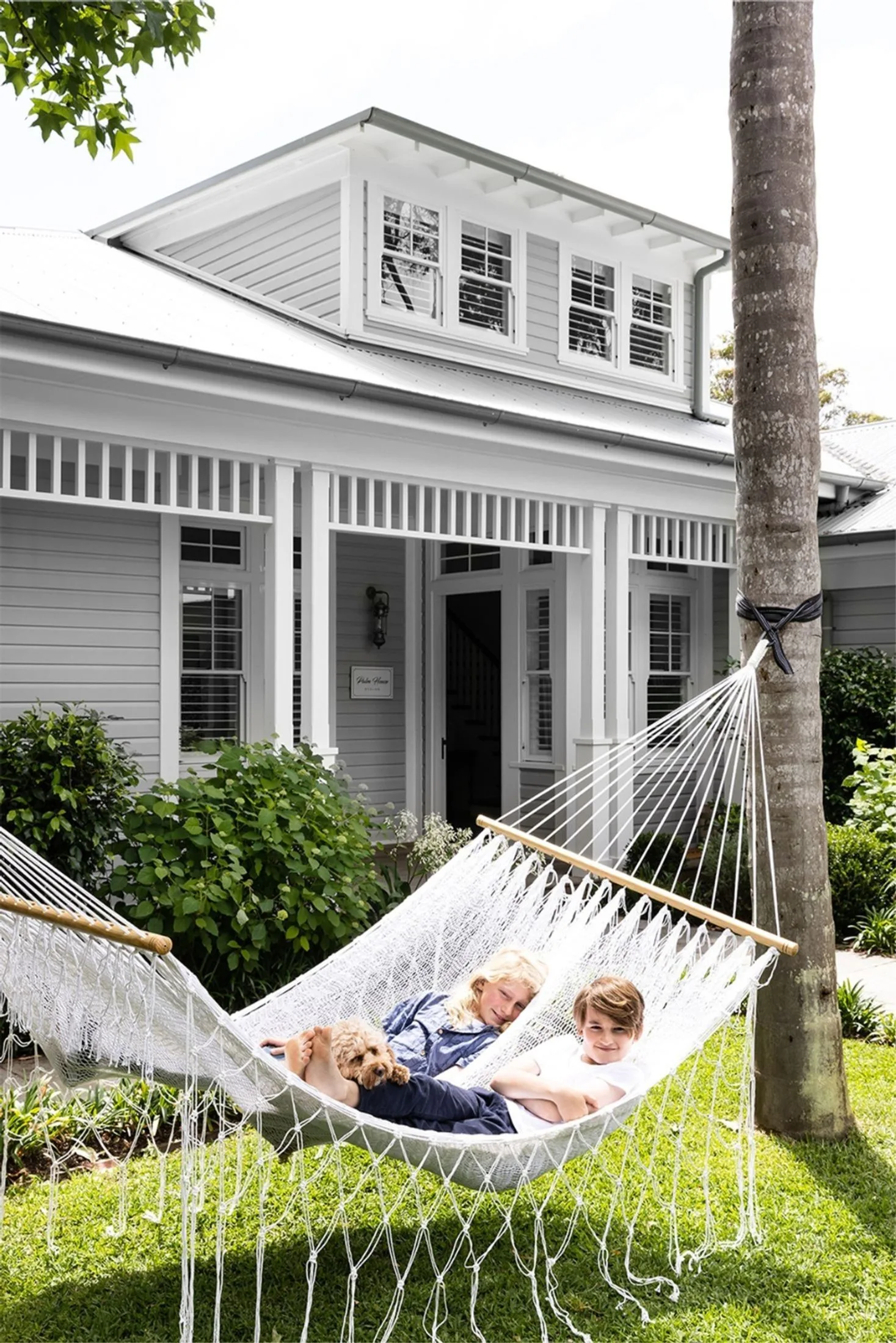 Children in hammock in the large backyard of a Hamptons style house