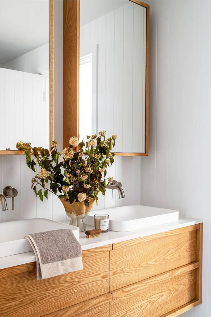 White and timber luxury bathroom styled with dried flowers, a candle and plush towel.