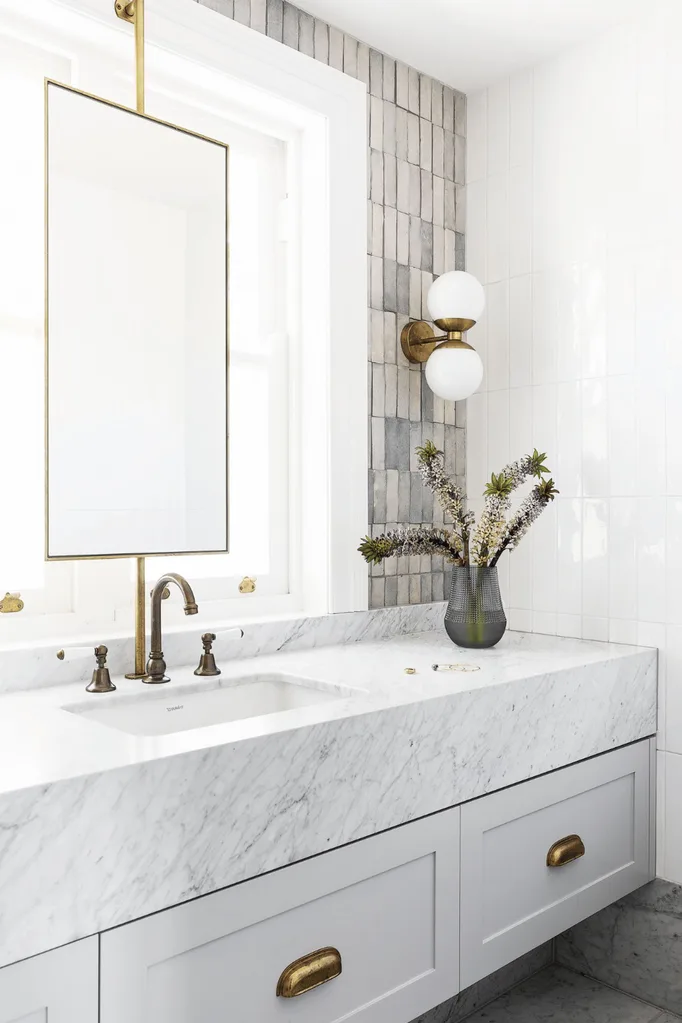 White and grey luxury bathroom with marble, brass hardware and a light sconce