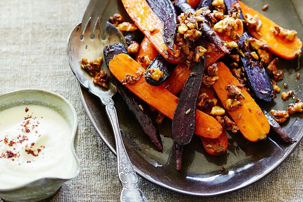 Roasted carrots with walnuts on a plate next to a bowl of creamy white dip, garnished with spices.