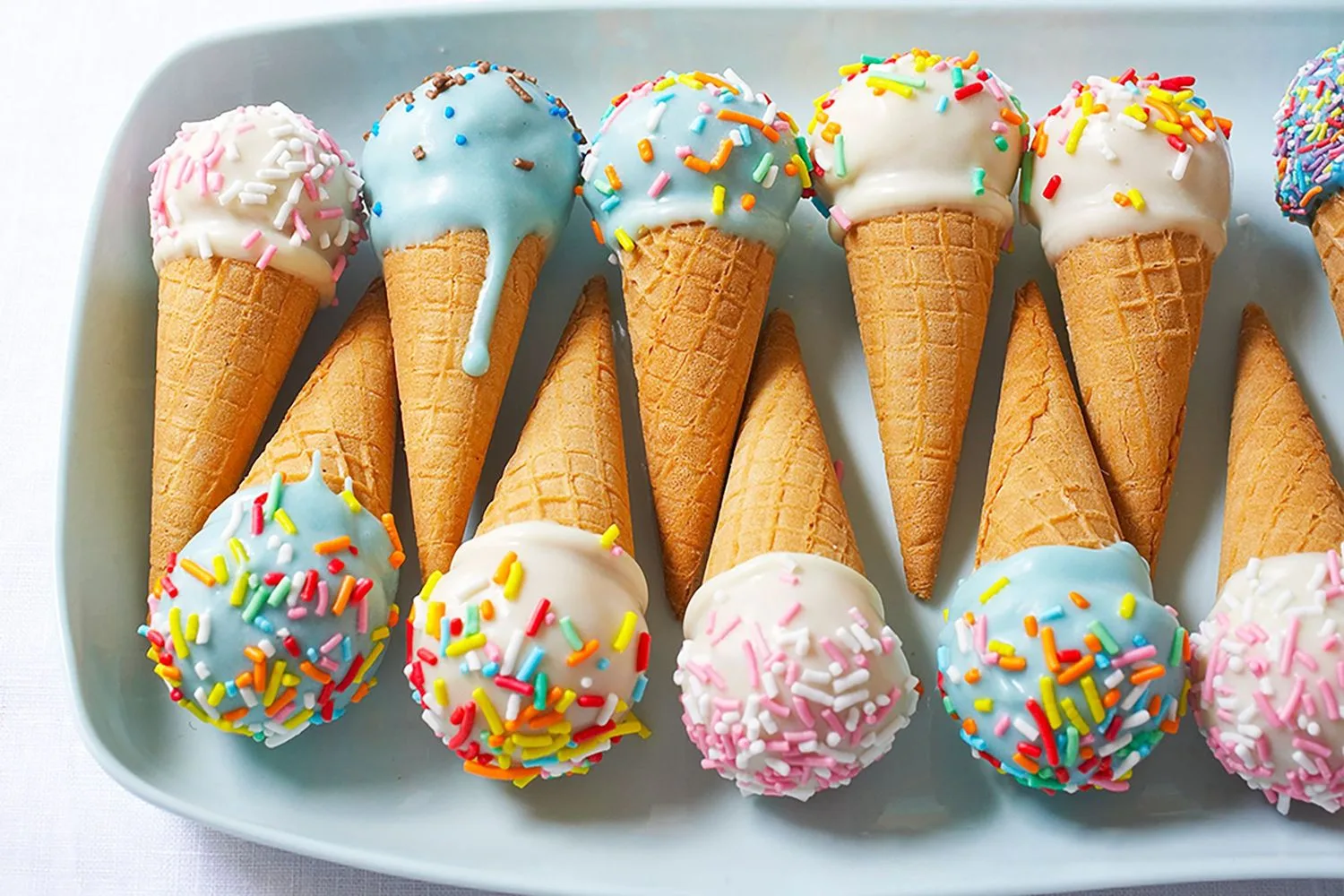 Mini ice cream cones with colorful sprinkles and blue or white topping on a white plate.