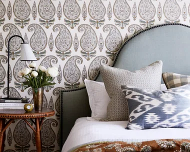Main bedroom with upholstered pale blue bedhead and paisley wallpaper